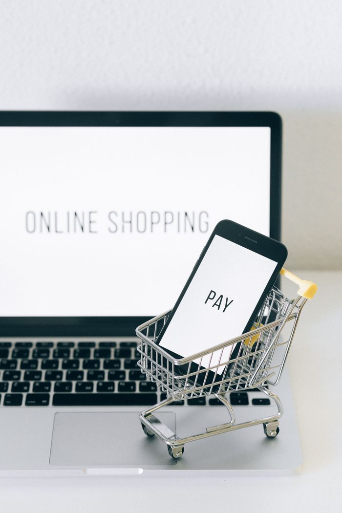 Pametni telefon u minijaturnoj korpi na laptopu simbolizuje online kupovinu i digitalno plaćanje.